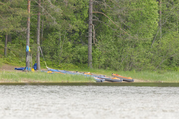 Inflatable kayaks and colorful paddles rest on a grassy lakeshore at the edge of a forest, prepared...