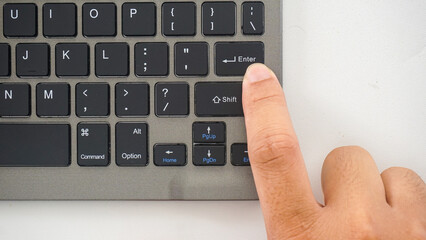 Top view of finger pressing enter button on a wireless computer keyboard isolated on white...