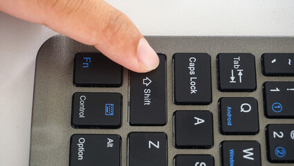 Finger pressing shift button on a wireless computer keyboard isolated on white background