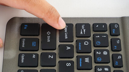 Finger pressing caps lock button on a wireless computer keyboard isolated on white background