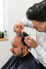 Hair transplant specialist attaching a hairpiece to a male client in a hair salon, using...