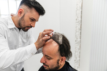 Hair specialist carefully applying a hair prosthesis to a patient, offering a non surgical solution...
