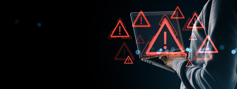 Cybersecurity warning symbols with exclamation marks hovering over laptop used by anonymous person in hoodie on dark digital background.