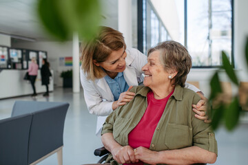 Geriatric doctor talking with patient in a wheelchair in hospital hallway.