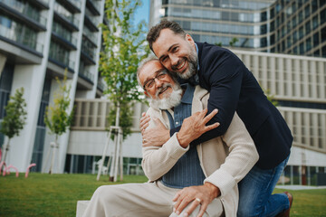 Father and adult son sitting on bench in park, sharing peaceful moment.