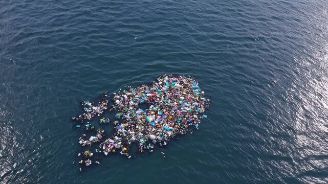 Aerial view of floating mass of ocean plastic and marine debris forming dense island in open water, representing environmental pollution, ocean crisis, and human impact on ecosystems
