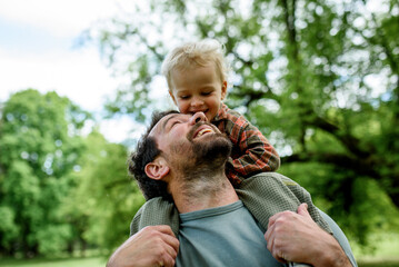 Father carrying his smiling son on shoulders during walk in park