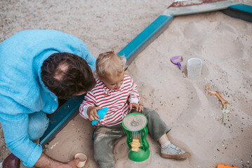 Naklejka premium Top view of dad and son playing in the sandbox on playground.
