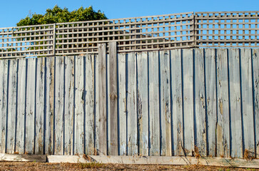 a deteriorating suburban timber fence with peeling paint and lattice screening on top.The aging...