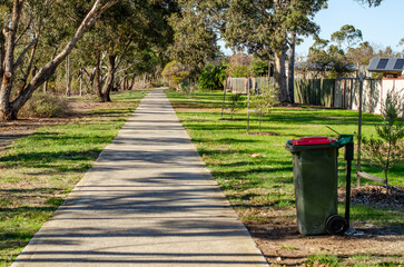 A concrete walking path runs straight through a green suburban corridor or public parkland lined...