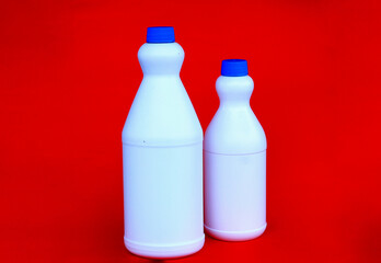 Plain white plastic bottle with blue cap, standing on bright red background. Cleanliness concept, industrial packaging product. Suitable for promotional themes and product advertising.