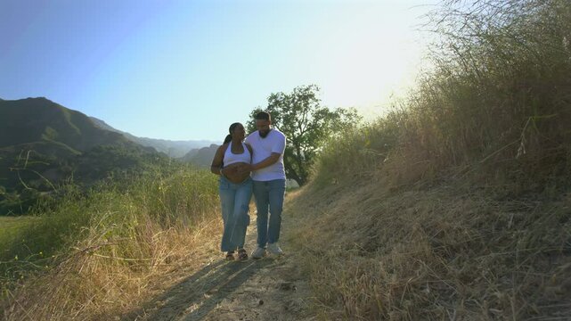 A beautiful pregnant African American couple is happily enjoying a lovely summer day outdoors, fully embracing each other while relaxing together in the beauty of nature surrounding them - Powered by Adobe