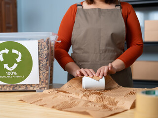 A woman is packaging a product using 100% reusable materials, supporting eco-friendly shipping, sustainability, waste reduction, and responsible consumption.