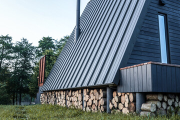 Modern A-frame cabin with vertical wood siding and a triangular window, viewed from a rustic wooden pathway leading to the front door