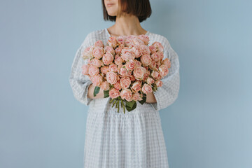 Lady in white dress embracing large cluster of soft pink roses in dreamy setting
