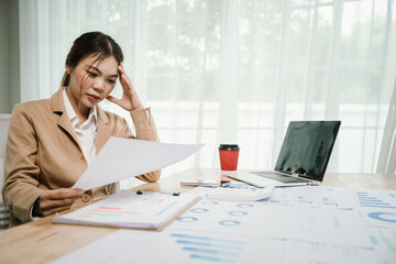 A poised young Asian businesswoman sits confidently at her modern home office desk, working remotely on a laptop, focused on finance, marketing, and professional growth.