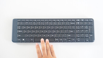 Top view of finger pressing space button on a black wireless computer keyboard isolated on white...