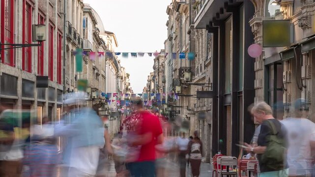 Tourists and locals walking and shopping in Rue Sainte-Catherine timelapse, Bordeaux, France. The longest pedestrian street in the country. Colorful flags decorate the street. Atmosphere of urban life
