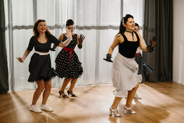 Four pinup dancers wearing polka dots are rehearsing rock and roll swing dance routine