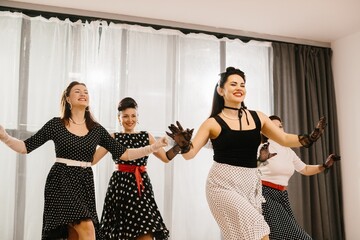 Four pinup women wearing polka dots dresses and gloves dancing in studio