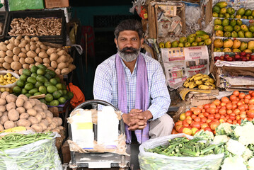 Indian shopkeeper man is selling green organic vegetables and fruits. Concept of self employment, farmer market, small business and agricultural entrepreneurship
