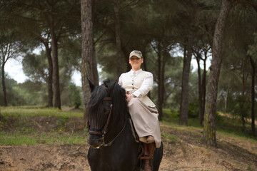 Young horsewoman riding her black Spanish thoroughbred horse, posing in the middle of the field....