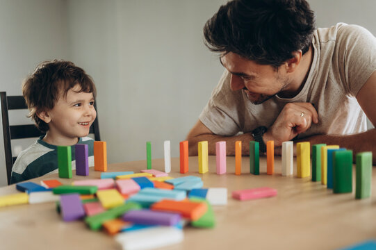 Father and son playing with colorful dominoes at home, smiling and bonding