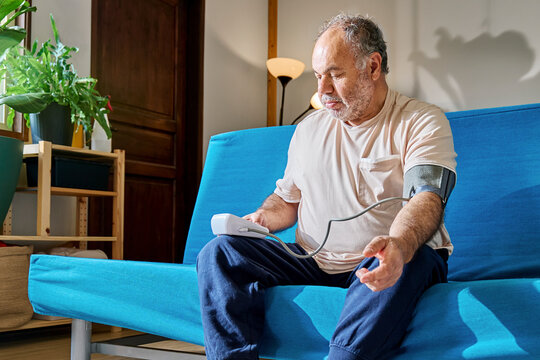 Senior man checking blood pressure at home on a sofa - Powered by Adobe