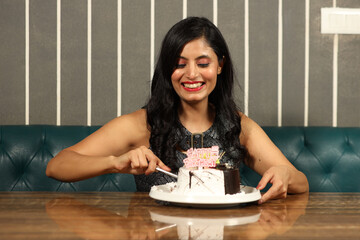 Indian young woman cutting cake in cafeteria 