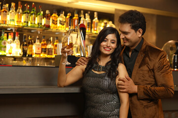 Indian loving couple toasting cocktail and beer glass at bar counter. Couple celebrating anniversary 