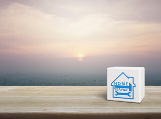 Hammer and wrench with house icon on white block cube on wooden table over modern city tower and skyscraper at sunset, vintage style, Business home service concept