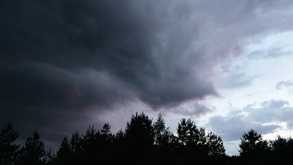 Fototapeta premium Dramatic thunderstorm with dark clouds in the evening. Dramatic cloudscape featuring dark, moody clouds with a bright, fiery orange glow