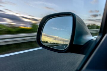 Car side mirror. Wind turbines on horizon. Speed and sustainability