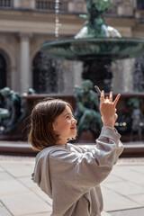 Girl photographing upward. Smartphone in hands. Fountain and architecture