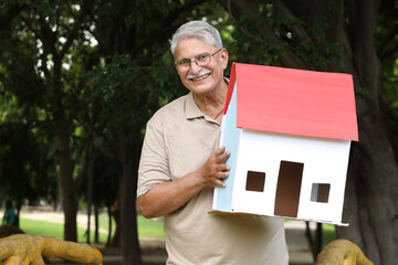 Portrait of Indian happy senior man  holding 3D paper home shape model in park - Concept - Real...