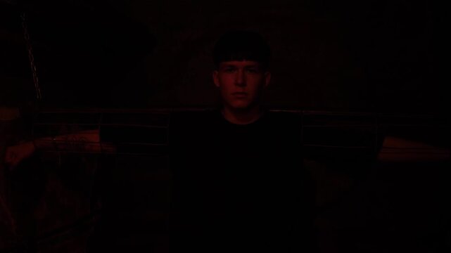 A young man is handcuffed to a wall in a dark room with a flashing red light, silhouette. A dark prison room with old rusty walls and antique shackles. The room of horrors. 
