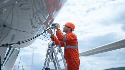 Aviation technician inspecting aircraft components while standing on a ladder at an airport during daytime