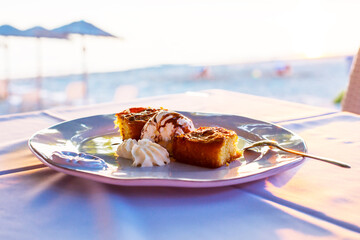 Two pieces of pie with ice cream in a white plate at the evening sun rays and beach umbrellas