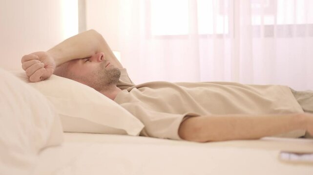 Tired Sleep-deprived young man lies in bed struggles with insomnia, unable to sleep. Sleep disorder, overthinking, restless thoughts deprivation, mental health, sleeping issues, disturbances