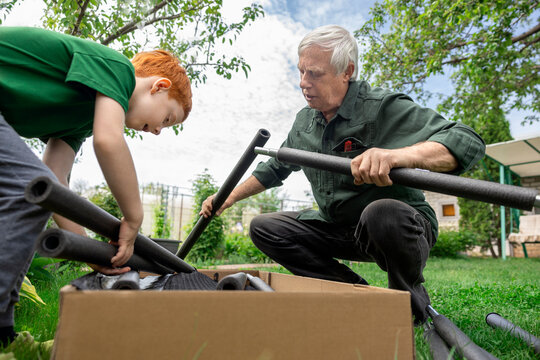 Elderly man and red-haired boy assembling a trampoline in the garden together
