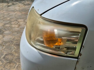 Close-up of an old car headlight with yellowed plastic and rust on the white body