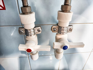 Utility valves with red and blue knobs are mounted on a tiled wall, indicating hot and cold water...