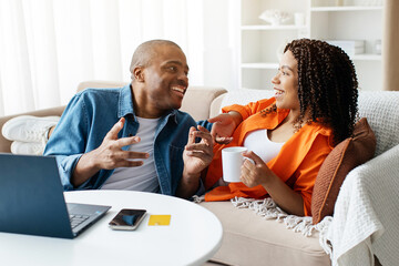 Cheerful Black Couple Relaxing Together With Laptop And Coffee In Living Room, Happy Young African...