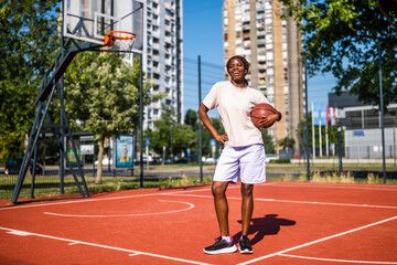 Obraz premium Young woman practicing basketball alone at sports court in the morning. Happy girl is ready for playing basketball on sunny day.