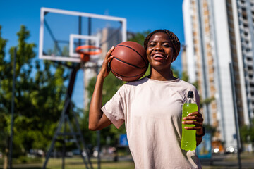 Young black woman practicing basketball alone at sports court in the morning. She is holding...