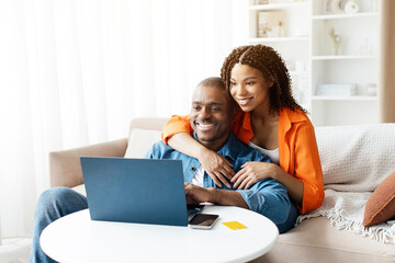 Smiling Black Spouses Spending Time With Laptop In Living Room, Happy African American Couple Using...