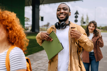 Students walking on campus with backpacks and folders, enjoying a sunny day at university