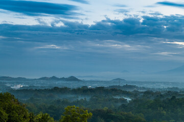 Scenic view of a tranquil forest and rolling hills with thin mist enveloping, the serene blue sky...