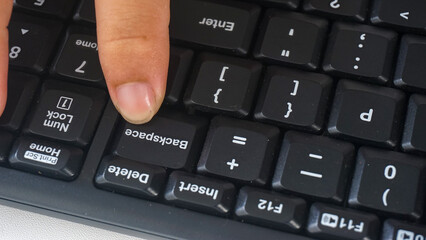 Finger pressing backspace button on a black modern wireless computer keyboard isolated on white...