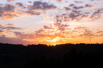 Vibrant Sunrise Over Hilly Terrain With Colorful Sky and Clouds. Golden sunlight illuminates a scenic hilly landscape while vivid orange and blue tones color the sky during sunrise.